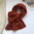Detail of burnt orange 100% wool scarf showing high-quality knit texture and tag - Orange