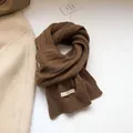 Close-up of dark brown 100% wool knitted scarf with textured cable stitch and white label - Coffee