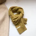 Macro shot of 100% wool ginger yellow cable knit scarf showing texture and material label - Mustard Yellow