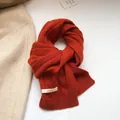 Close-up of 100% wool orange cable knit scarf with visible washing label and soft texture - Orange Red