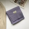 Detail of purple wool knit scarf with ribbed edge and woven label on a lifestyle layout - Lavender