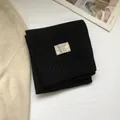 Detailed close-up of 100% pure wool scarf with ribbed edges and fabric composition label - Black