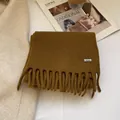 Detail showing 100% wool material tag and soft fringe texture on a mustard yellow scarf - Bronze