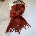 Close-up of caramel wool knit scarf featuring fringe tassels and a silver metal logo tag - Orange