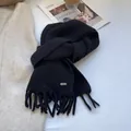 Detail of a black knitted wool scarf with long tassels and a small metal logo plaque - Black
