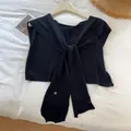 Detail view of black knitted shawl with tie-front knot and ribbed edges on hanger - Black