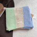 Detailed texture of a tri-color knit scarf with logo patch on soft plush background - Milky Green Apricot Baby Blue
