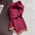 Macro detail of wool blend scarf featuring burgundy knit and golden logo emblem - Burgundy