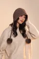 Detailed close-up of dark brown wool knit hat with diamond patterns and plush pom-poms - Khaki
