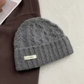 Detail der Strickstruktur einer grauen Wollmütze mit Zopfmuster und 100% Wolle Textiletikett - Grau