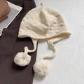 Detailed knit texture of a cream pumpkin-style hat with fluffy pompoms and earflaps - Cream Rice