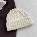 Detail einer grob gestrickten Beanie aus 100% Wolle mit Etikett und Strickstruktur - Creme