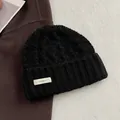 Detail einer schwarzen Strickmütze aus 100% Wolle mit grobem Zopfmuster und weißem Etikett - Schwarz