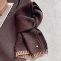 Detailed close-up of dark brown wool blend scarf with ribbed edges and metallic logo tag - Coffee