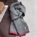 Detail of wool blend scarf with red scalloped edge and gold logo pin on grey fabric - Dark Gray