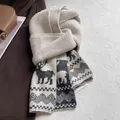 Detail eines cremefarbenen Strickschals mit Rentier-Muster und Leder-Logo-Etikett im Fokus - Jacquard-Rentier-Stil / Gebrochenes Weiß