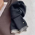 Close-up of black wool blend scarf with white stripes and round gold metal tag detail - Black