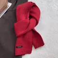 Close-up of red 100% wool knitted scarf with flecked details and fabric care label - New Year Red