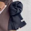 Detailaufnahme des schwarzen Wollmischschals mit feiner Stricktextur und Studio-Webetikett - Schwarz