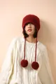 Detalle de un gorro de lana de punto rojo oscuro con orejeras y pompones decorativos - Rojo