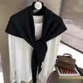 Detailed close-up of a black knitted shawl with a white logo label on the end - Black