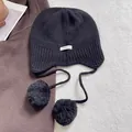 Detalle del gorro de punto de lana negra con pompones y etiqueta de material 100% lana - Negro