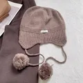 Detalle de gorro de punto 100% lana con orejeras suaves y pompones decorativos de felpa - Caqui