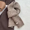 Close-up of a thick speckled knit wool scarf with a minimalist white label on dark fabric - Coffee