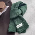 Detail showing the thick cable knit texture and white brand label on the dark green scarf - Green
