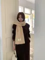 Dettaglio di sciarpa beige lavorata a maglia a mano con etichetta tessuta Bonnie - Albicocca