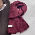 Deep burgundy chunky knit scarf with white woven label on soft textured background - Red