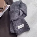 Detailed close-up of thick cable knit texture and fabric label on a winter scarf - Gray