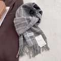 Detailweergave van grijze geruite wollen sjaal met zachte franjes en merklabel - Schotse Ruit