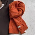Gros plan d'une écharpe orange en pure laine avec maille torsadée et étiquette textile - Orange