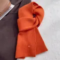 Detail of bright orange wool knit scarf texture and small oval metal brand tag - Bright Orange