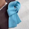 Detail eines hellblauen Wollschals mit Rippenstrickmuster und ovalem Logo-Metall-Tag - Gletscherblau