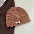 Detailed macro view of 100% wool label on the crochet knitted beanie with hollow patterns - Bright Orange
