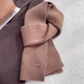 Close-up of dark brown ribbed knit wool scarf texture with small oval detail tag - Caramel color