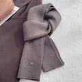Detail view of the ribbed knit wool texture and metal brand tag on the brown scarf - Grey Coffee