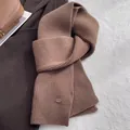 Detailansicht eines braunen Wollschals mit Grobstrickmuster und einer Metallschnalle - Karamellbraun