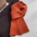 Detail eines orangefarbenen Wollschals mit vertikalem Rippmuster und Logo-Knopf - Helles Orange