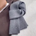 Detail of the grey knitted wool scarf showing rib-knit texture and elegant oval brand tag - Gray