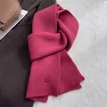 Detail eines magenta Schals aus reiner Wolle mit vertikaler Streifenstruktur und Logo - Scharlachrot