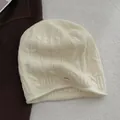 Detail der Zopfstrickstruktur und des 100% Wolle-Etiketts an einer beigen Mütze - Gebrochenes Weiß