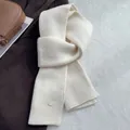 Detail of cream white ribbed knit wool scarf with a decorative oval metal logo tag - Cream Rice