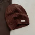 Nahaufnahme der dunkelbraunen Strickmütze aus 100 % Wolle mit Zopfmuster und Textiletikett - Kaffeebraun