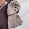 Close-up of light brown ribbed knit wool scarf with elegant oval metal charm detail - Camel