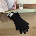 Close-up of black knitted gloves featuring grey ribbed cuffs and a white fabric brand label - Black