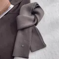 Detailaufnahme des dunkelbraunen Wollschals mit feinem Rippenstrick und Metall-Logo-Tag - Grau Kaffee
