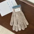 Detail of light brown knit gloves with blue ribbed cuffs and brand label on wood - Milk Tea